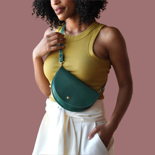 Woman wearing a yellow top and white pants with a green crossbody bag against a brown background