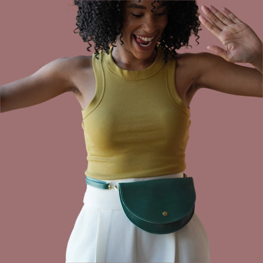 A person wearing a yellow tank top and white pants, accessorized with a green leather hip pack with a suede interior, attached to an adjustable strap.